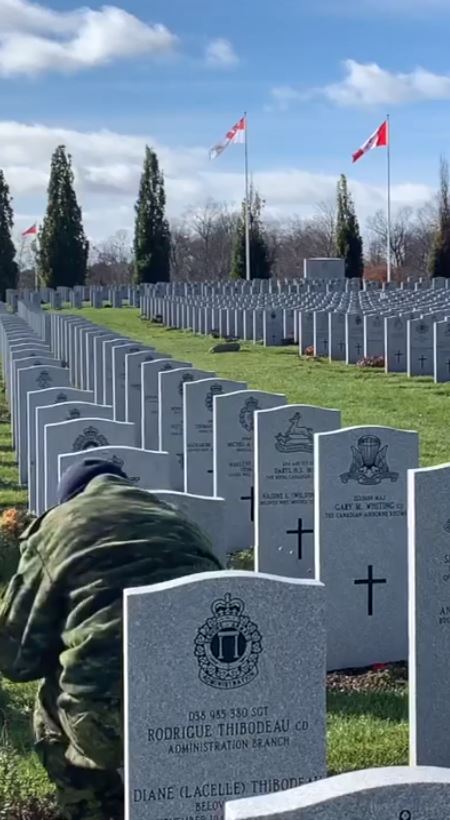 Soldier kneeling in front of grave placing poppy
